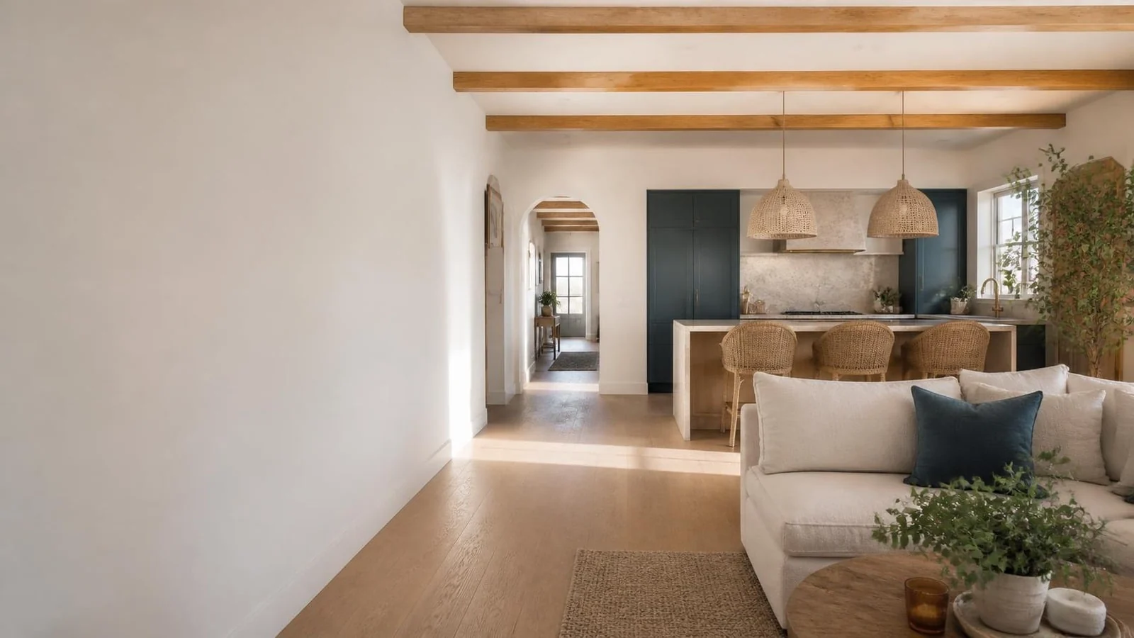 Salón luminoso con vigas de madera clara, abierto a una cocina moderna con lámparas colgantes y suelo de madera en espiga